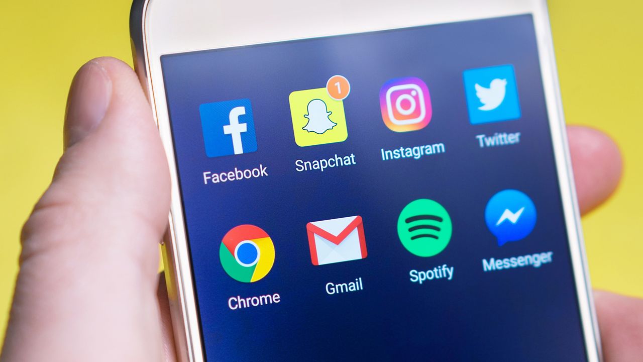 A person’s hand holding a smartphone that shows social media and messaging apps.